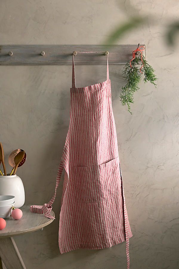 a pink striped apron hanging on a wall next to a white vase with flowers and utensils