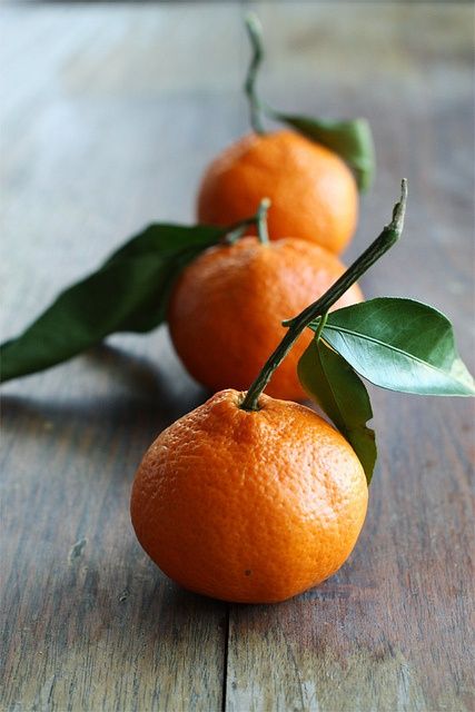 three oranges with green leaves on them sitting on a wooden table