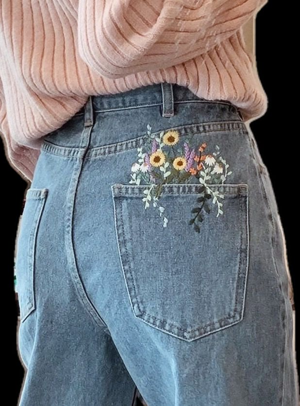 the back of a woman's jeans with flowers embroidered on it and an open pink sweater