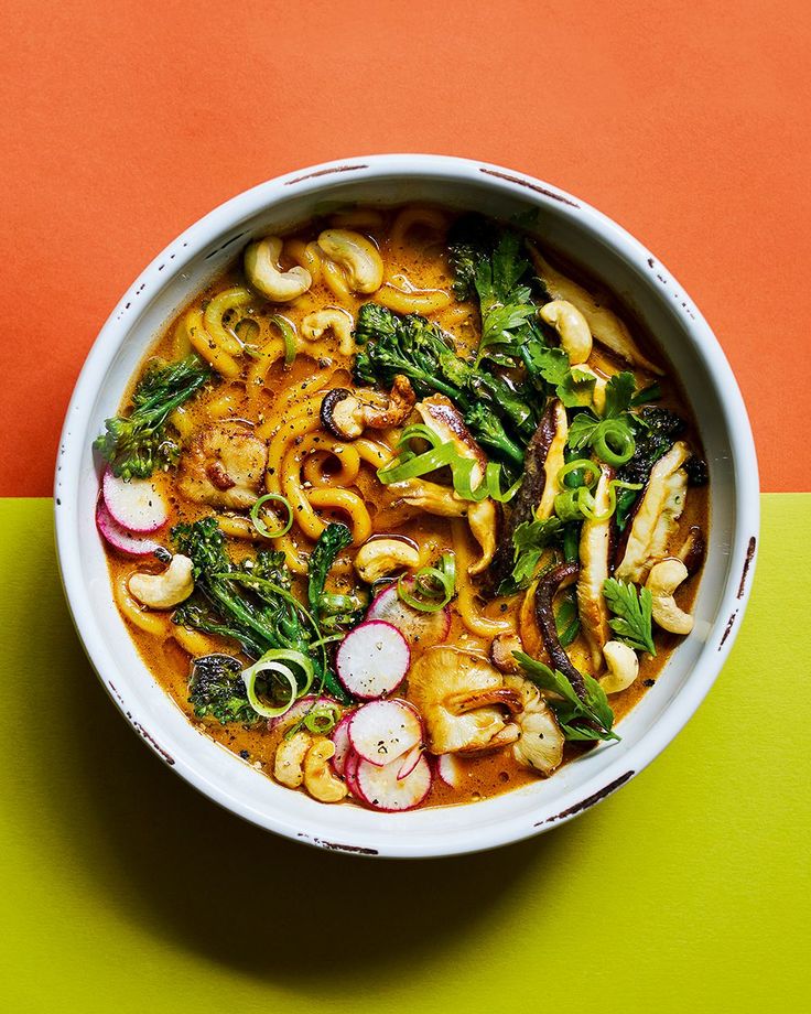 a white bowl filled with noodles, broccoli and other vegetables on top of a green and orange table