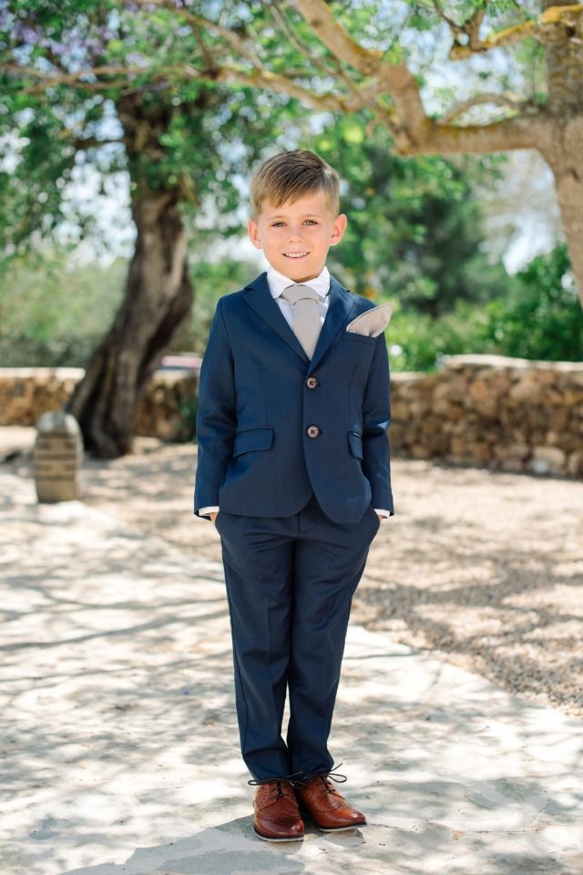 a young boy in a suit and tie standing on a stone path under a tree