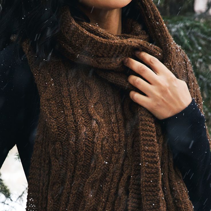 a woman wearing a brown scarf and black jacket in the snow with her hands on her chest