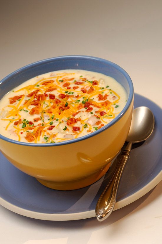 a bowl of soup with bacon and cheese in it on a blue plate next to a silver spoon