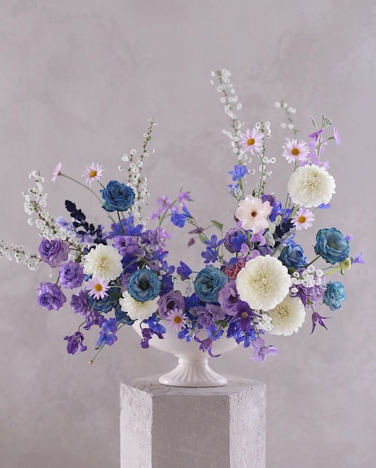 a white vase filled with lots of purple and white flowers on top of a table