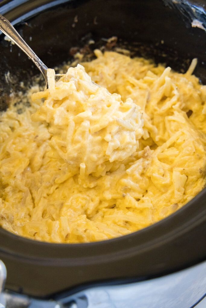 a crock pot full of macaroni and cheese being stirred with a ladle