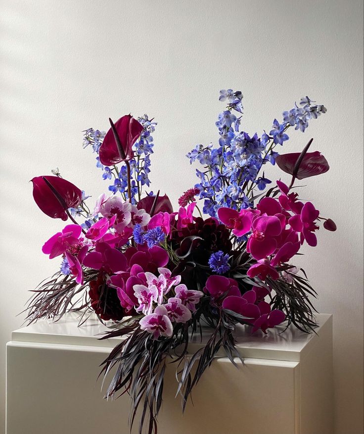 a vase filled with lots of purple and blue flowers on top of a white table