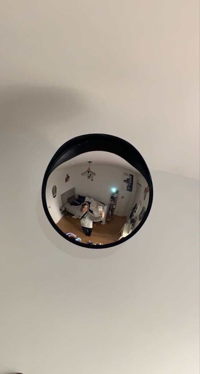 a mirror hanging from the side of a white wall next to a bed and desk