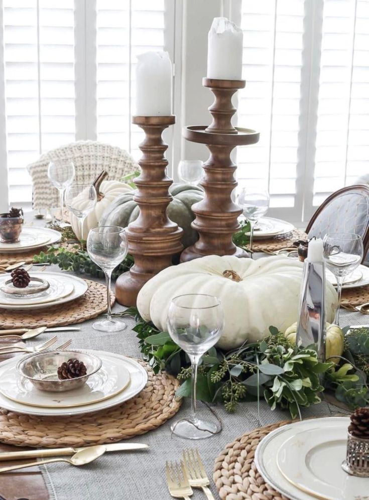 the table is set for thanksgiving dinner with white pumpkins, greenery and candles