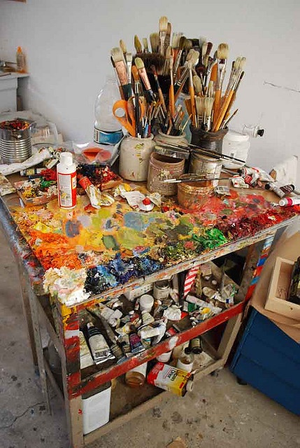 an artist's desk with lots of paint and brushes