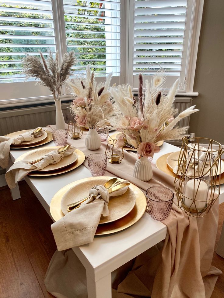 the table is set with plates, napkins and vases filled with dried flowers