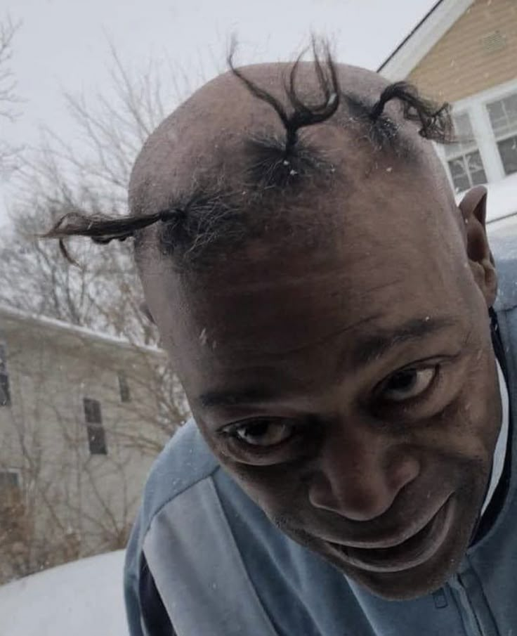 a balding man with long hair standing in front of a house on a snowy day