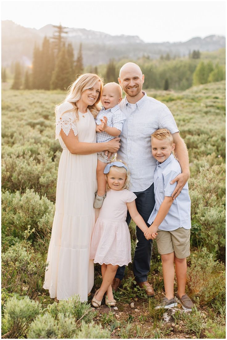 a family posing for a photo in the grass with mountains in the background at sunset