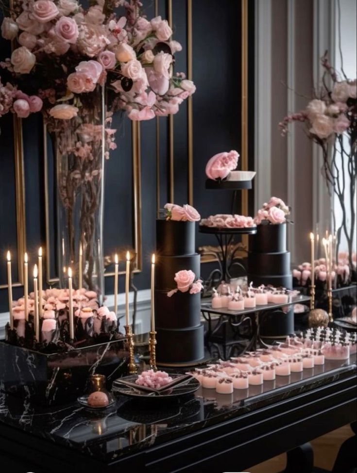 a black table topped with lots of pink flowers and cupcakes on top of it