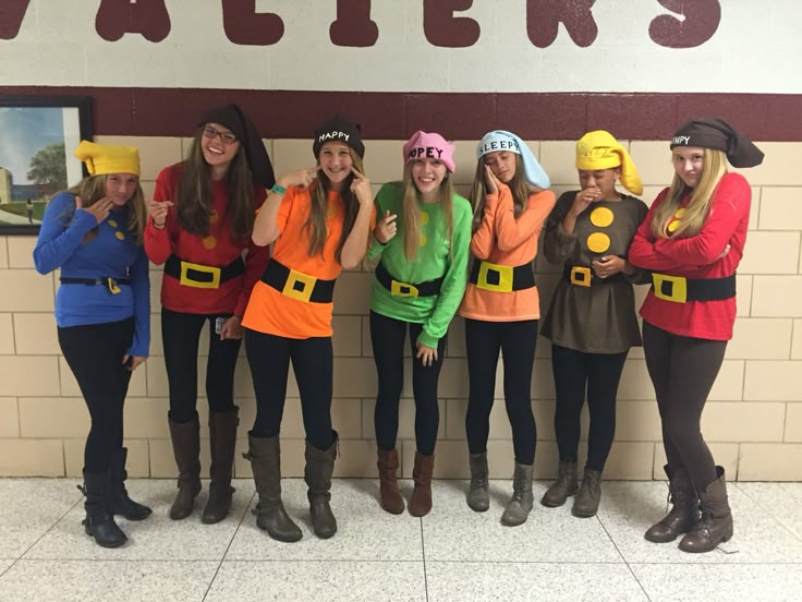 a group of women standing next to each other in front of a wall wearing costumes