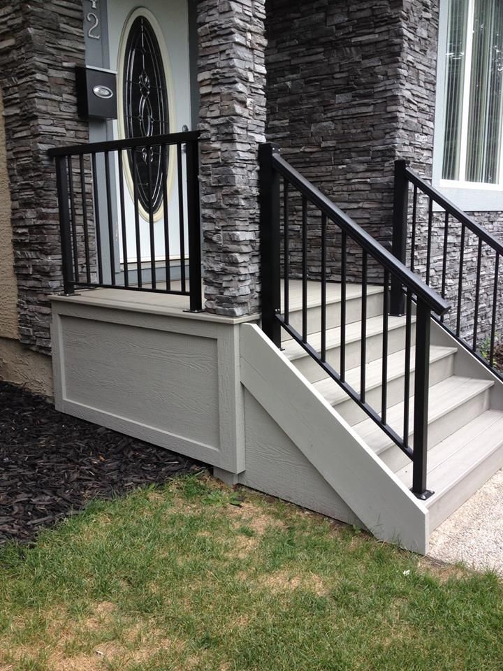 a front porch with black iron railings and stone pillars on the side of a house