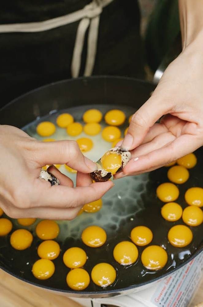 two hands reaching for an egg in a frying pan with other eggs on it