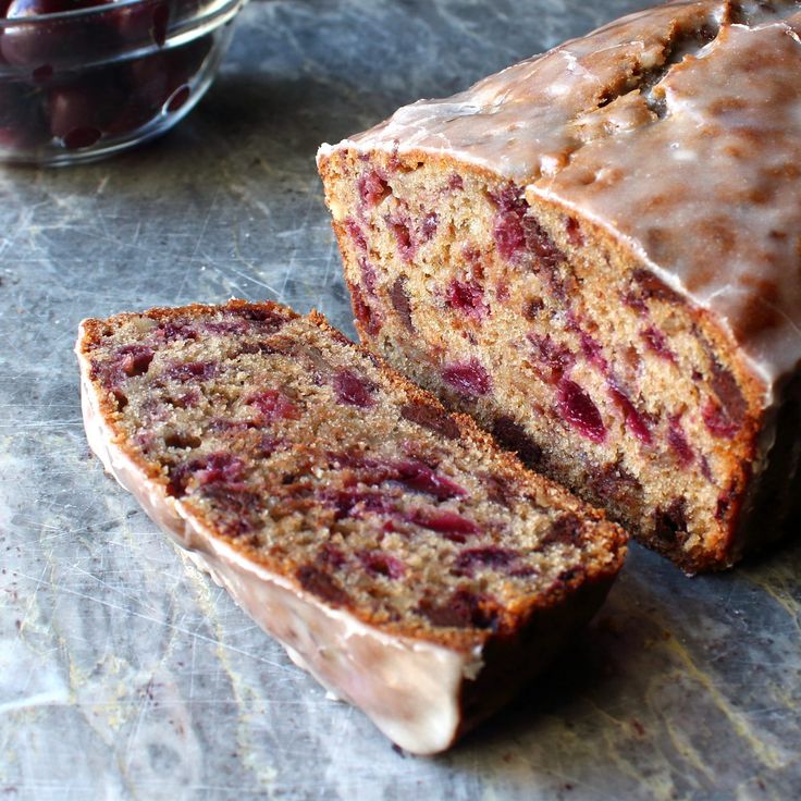 there is a loaf of cake with chocolate icing on the top and cherries in the background