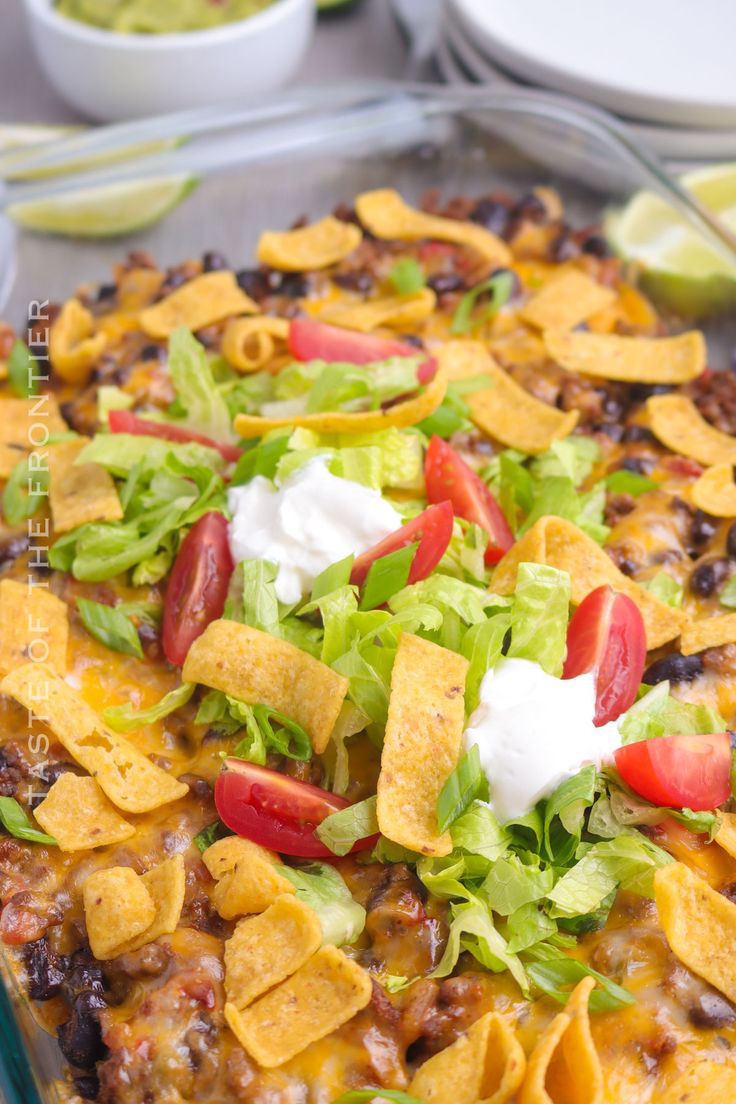 a casserole dish with tortilla shells, lettuce and tomatoes