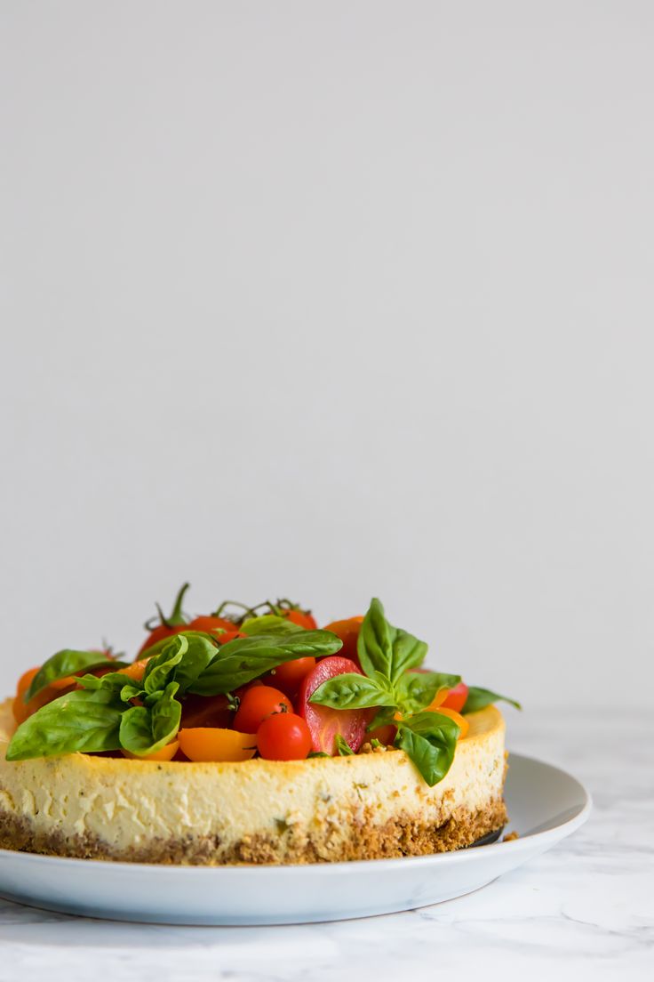 a white plate topped with a cheesecake covered in veggie toppings on top of a marble counter