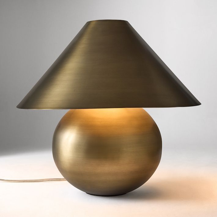 a gold lamp with a black shade on the bottom and a white background behind it