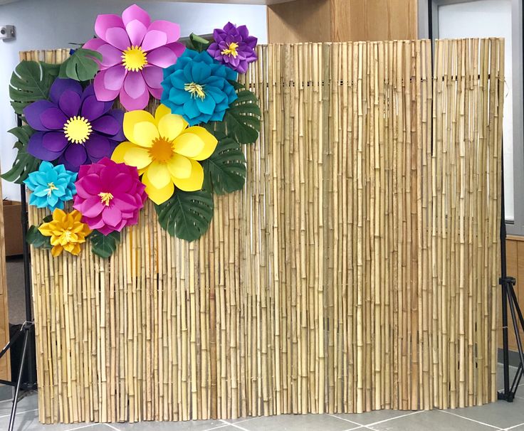 colorful paper flowers are placed on the bamboo wall in front of an empty room with chairs