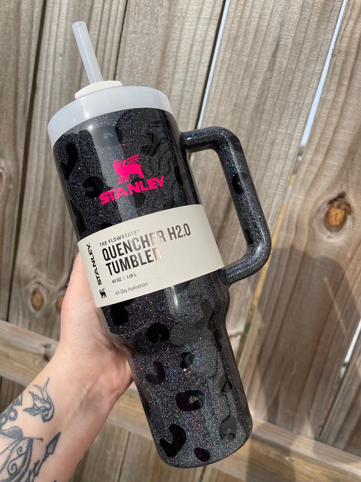 a hand holding a black glittered tumbler cup with a pink logo on it