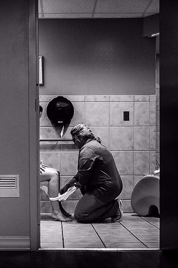 a man sitting on the floor in front of a bathroom door while shaving his leg