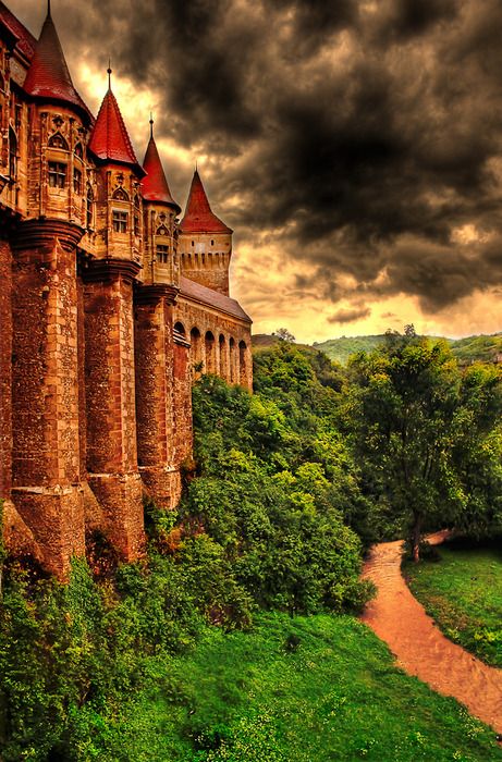 an old castle is surrounded by lush green trees and grass, under a cloudy sky