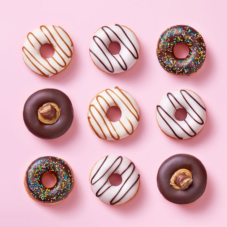 six donuts with chocolate frosting and sprinkles arranged on a pink background