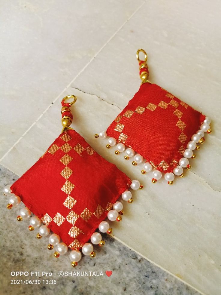 two red and gold earrings with pearls hanging from the ends of each earring, on a marble surface