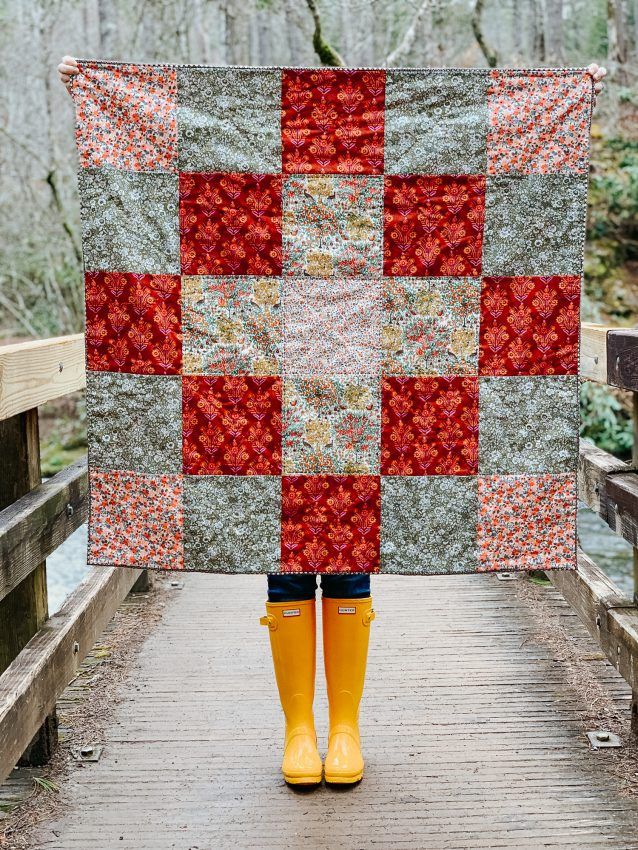 a woman in yellow rubber boots holding up a quilt