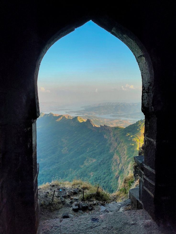 an arch in the side of a mountain with a view of mountains and valleys below