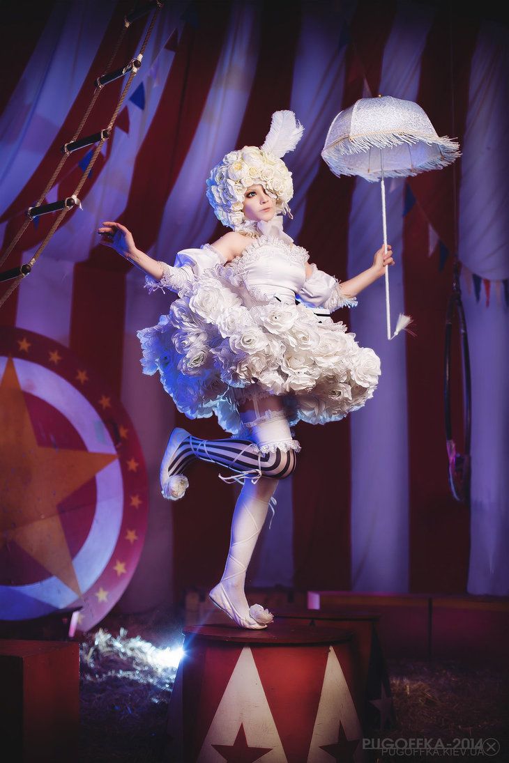 a woman dressed in white and holding an umbrella on top of a wooden platform with flags behind her