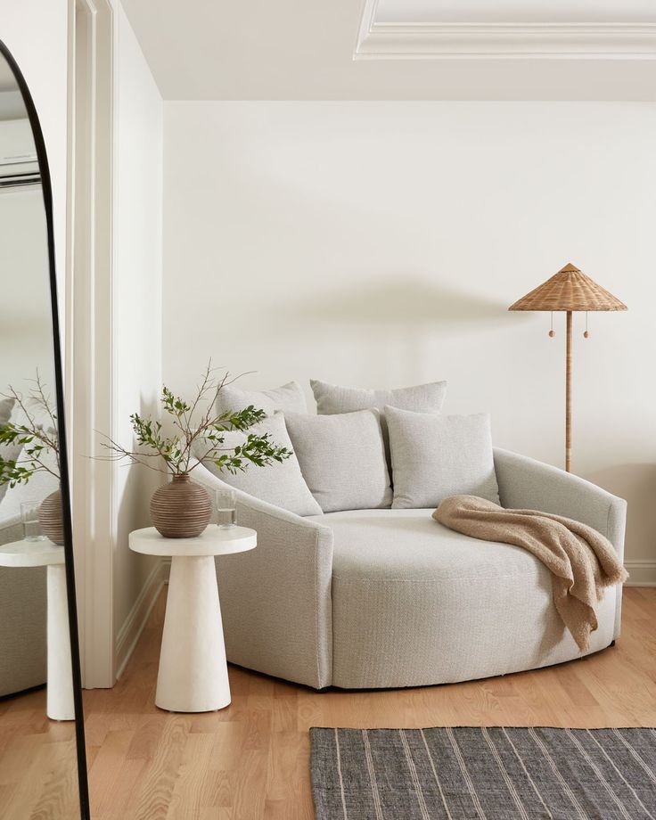 a white couch sitting on top of a hard wood floor next to a mirror and table