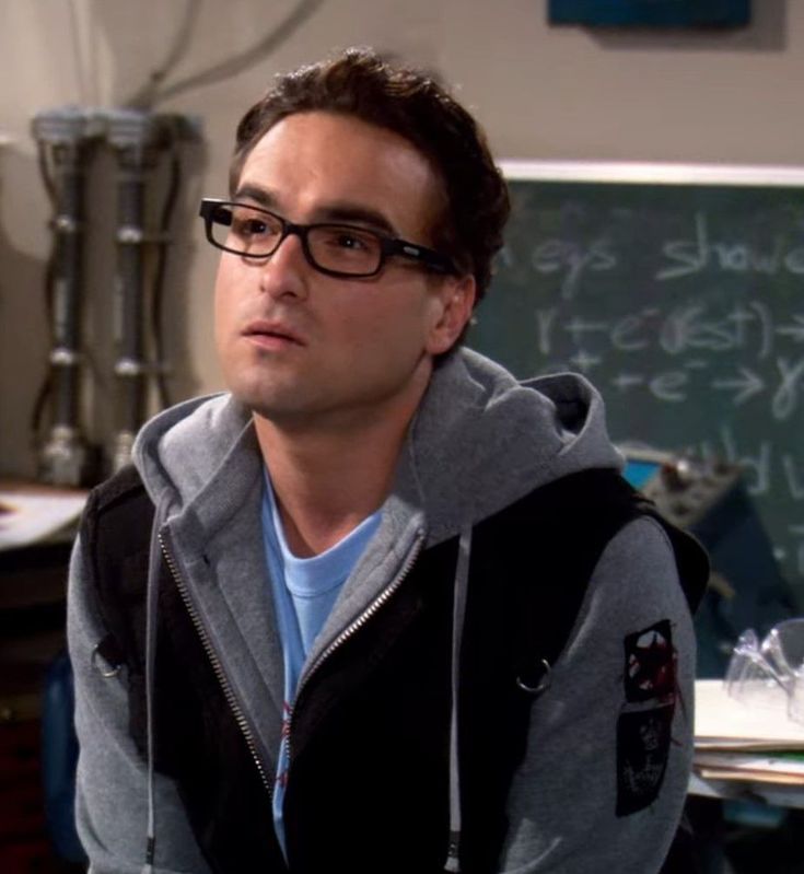 the young man is wearing glasses in front of a chalkboard with writing on it