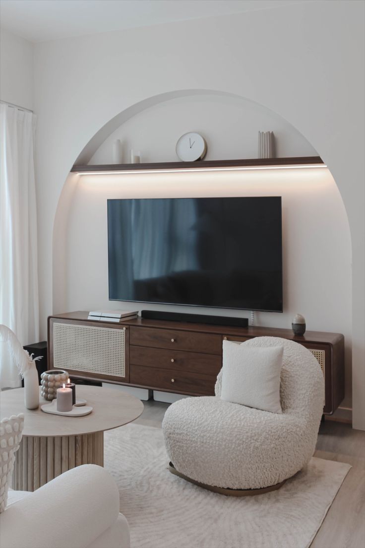 a living room with white furniture and a large flat screen tv mounted on the wall