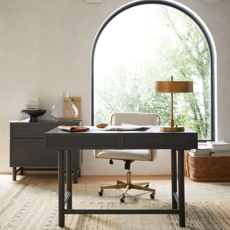 a desk with a chair and lamp in front of an arched window