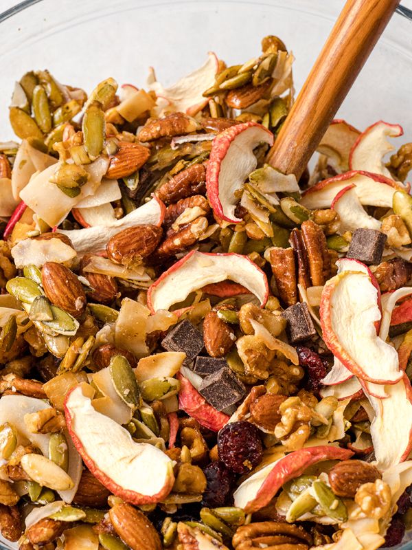 a glass bowl filled with nuts, apples and cranberry mixture next to a wooden spoon