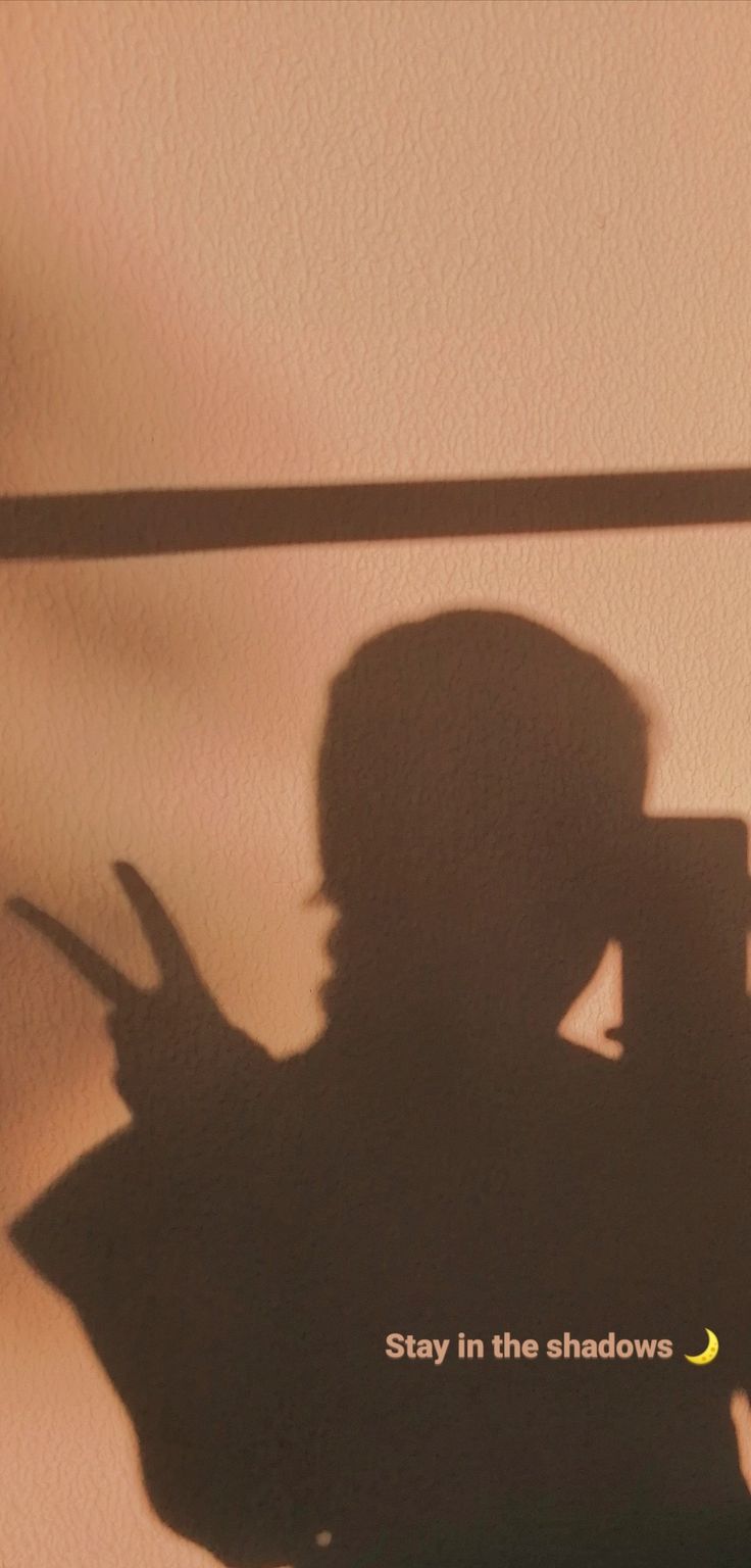 the shadow of a person holding a cell phone up to their face, with text that reads stay in the shadows