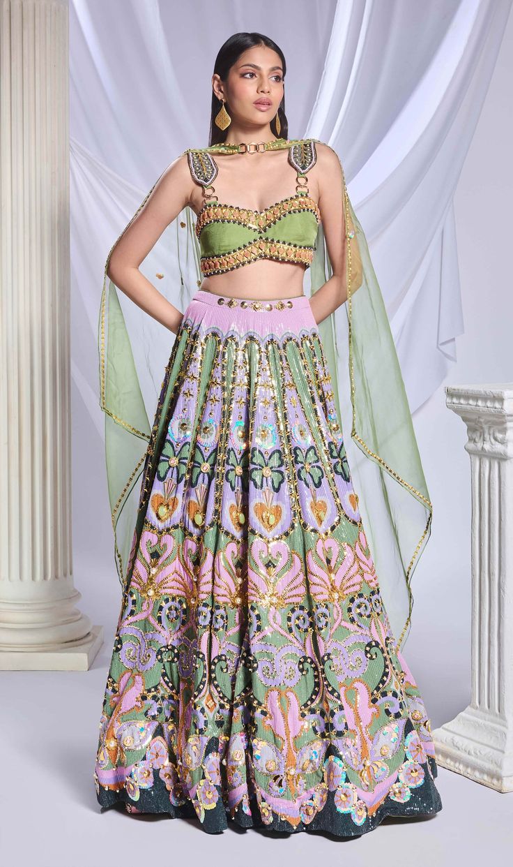 A green sequin-printed lehenga featuring pockets, adorned with gold chains, crystals, pearls and heart-shaped metal accents. It is paired with a green organza blouse, embroidered with gold chains, pearls, glass stones and beads, along with an asymmetrical organza dupatta with a pearl border and sequin scatter. Festive Embellished Green Sharara, Festive Green Embellished Sharara, Anarkali Embellished Green Choli, Green Embellished Anarkali Choli, Anarkali Style Embellished Green Choli, Embellished Green Lehenga For Festive Occasions, Festive Embellished Green Lehenga, Festive Green Embellished Lehenga, Green Silk Sets For Reception