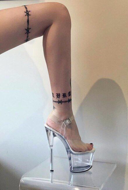 a woman's legs with cross tattoo on her left leg and clear high heels