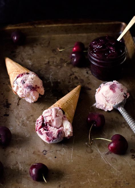 three ice cream cones with cherries on a baking sheet next to a jar of jam