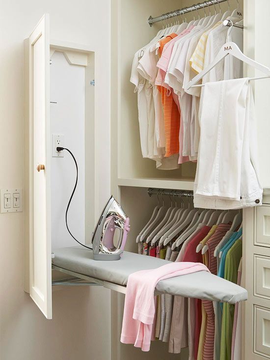 an ironing board and clothes hanging on a rail in a closet with white drawers