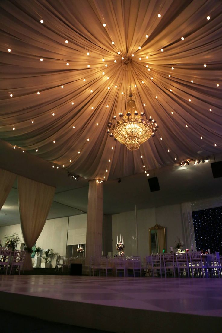 the ceiling is decorated with lights and draping for a wedding reception at night