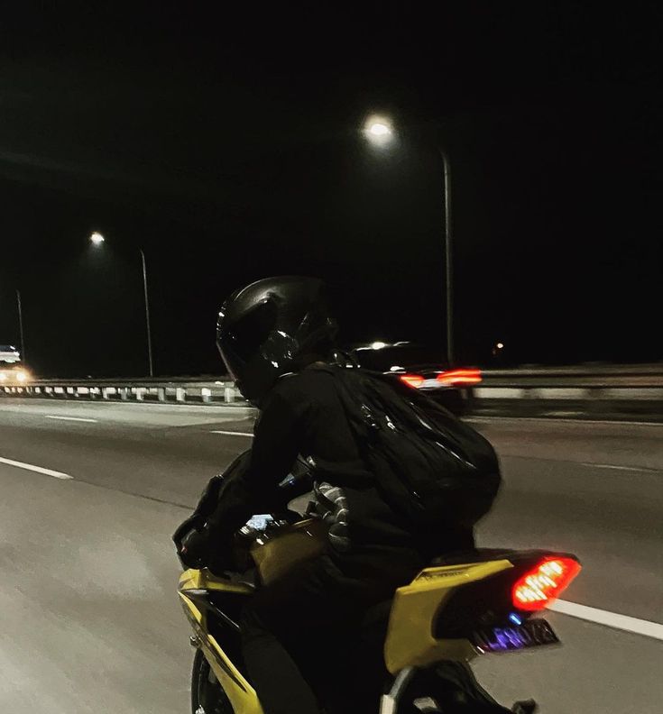 a man riding on the back of a yellow motorcycle down a street at night time