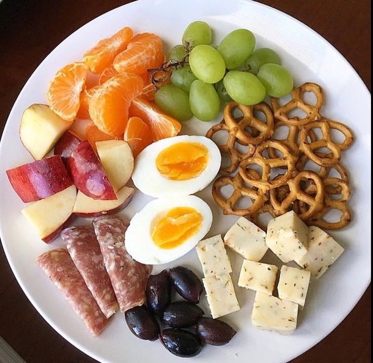 a white plate topped with fruit and crackers next to an egg, oranges, grapes