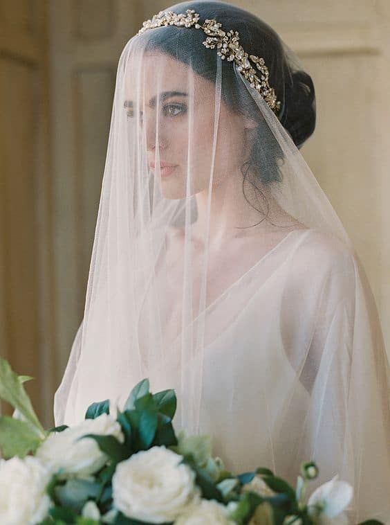 a woman wearing a wedding veil and holding a bouquet in front of her face while looking at the camera