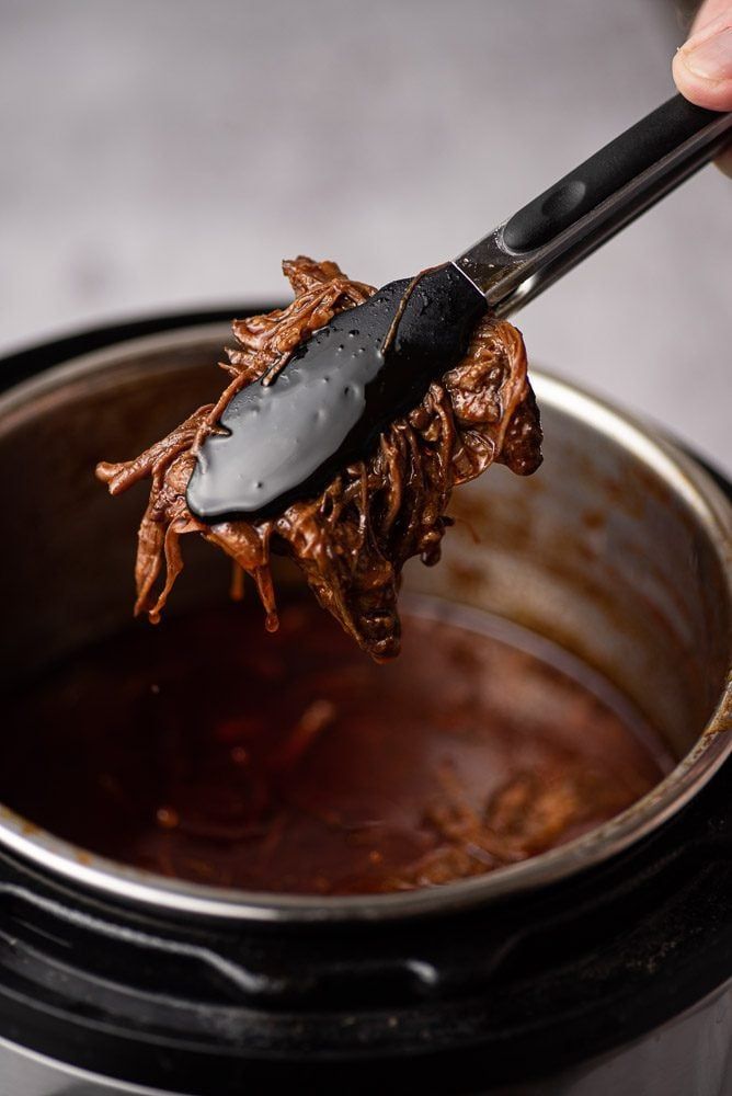 a person is spooning some food out of a crock pot with it's lid open