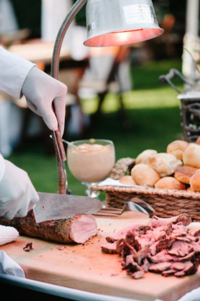 a person in white gloves is cutting meat on a table with bread and other foods