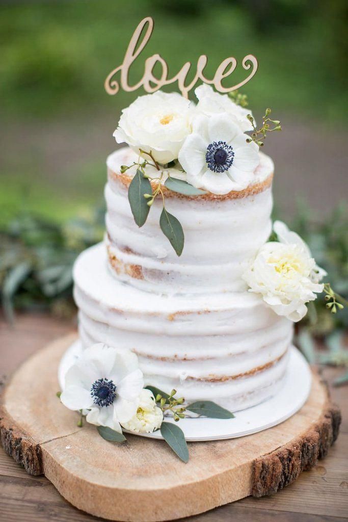 a wedding cake with white flowers and the word love on top is sitting on a wooden slice